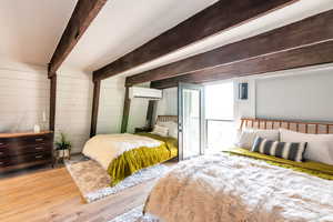 Bedroom featuring wooden walls, a wall mounted air conditioner, beam ceiling, and light hardwood / wood-style flooring