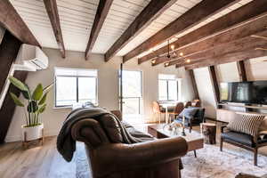 Living room featuring a healthy amount of sunlight, beam ceiling, light hardwood / wood-style floors, and an AC wall unit