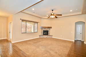 Unfurnished living room featuring ceiling fan, dark wood-type flooring, a stone fireplace, and a raised ceiling