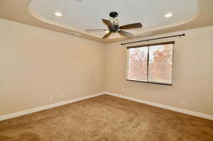 Spare room featuring ceiling fan, carpet flooring, and a raised ceiling