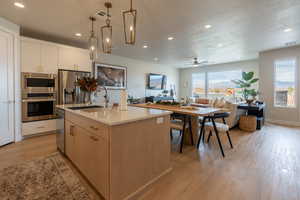 Kitchen with appliances with stainless steel finishes, sink, light hardwood / wood-style floors, hanging light fixtures, and a kitchen island with sink