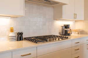 Kitchen with white cabinetry, stainless steel gas cooktop, backsplash, light stone counters, and wall chimney range hood