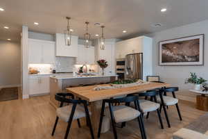 Kitchen with appliances with stainless steel finishes, an island with sink, decorative backsplash, pendant lighting, and white cabinetry