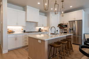 Kitchen with appliances with stainless steel finishes, sink, white cabinetry, hanging light fixtures, and a kitchen island with sink