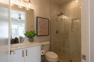 Bathroom with vanity, ceiling fan, a shower with shower door, and toilet