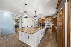 Kitchen with built in microwave, custom range hood, white cabinets, decorative light fixtures, and a spacious island