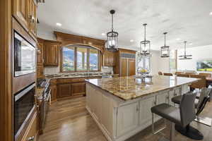 Kitchen with light stone counters, stainless steel microwave, a center island, oven, and a kitchen bar