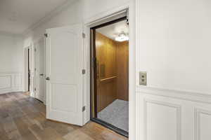 Hall with elevator, hardwood / wood-style flooring, and crown molding