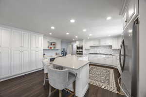 Kitchen with a center island with sink, a kitchen bar, white cabinetry, dark hardwood / wood-style floors, and stainless steel appliances