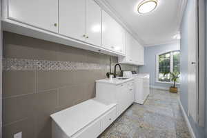 Washroom with washing machine and dryer, cabinets, sink, and ornamental molding