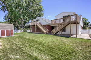 Rear view of house featuring a deck, a patio area, a lawn, and a storage shed