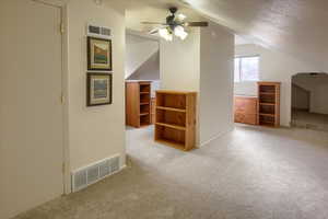 Bonus room with ceiling fan, a textured ceiling, light colored carpet, and lofted ceiling