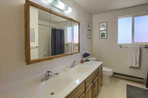 Bathroom featuring a baseboard radiator, toilet, vanity, and a healthy amount of sunlight