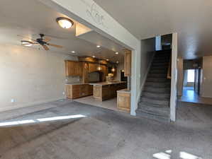 Unfurnished living room with baseboards, light carpet, stairway, a textured ceiling, and a ceiling fan