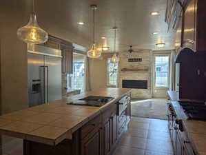 Kitchen featuring a center island, open floor plan, a ceiling fan, stainless steel appliances, and tile countertops