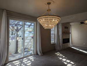 Unfurnished dining area with ceiling fan with notable chandelier, carpet flooring, baseboards, and a large fireplace
