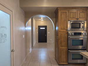 Kitchen featuring light tile patterned floors, baseboards, arched walkways, brown cabinetry, and stainless steel appliances