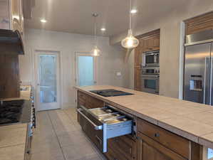 Kitchen with built in appliances, a warming drawer, light tile patterned flooring, decorative light fixtures, and brown cabinets