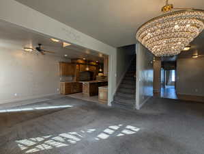 Unfurnished living room featuring ceiling fan with notable chandelier, a textured ceiling, light carpet, stairs, and baseboards
