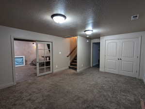 Finished below grade area with baseboards, a textured ceiling, carpet floors, stairs, and visible vents