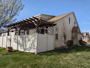 View of side of property featuring a pergola, fence, and a lawn