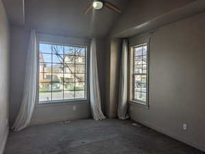 Carpeted spare room with visible vents, a ceiling fan, plenty of natural light, and vaulted ceiling