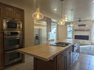 Kitchen featuring a textured ceiling, tile countertops, built in appliances, and a fireplace