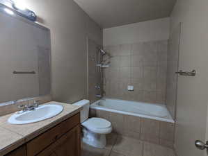 Full bath featuring a textured ceiling, vanity, tile patterned flooring, toilet, and tiled shower / bath combo