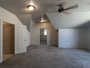 Primary bedroom featuring baseboards, ceiling fan, carpet, a textured ceiling, and vaulted ceiling