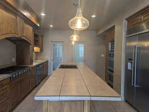 Kitchen featuring built in appliances, a sink, tile counters, a kitchen island, and tile patterned flooring