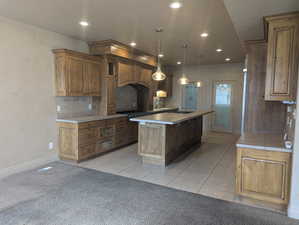 Kitchen with custom range hood, light carpet, a center island, light countertops, and gas stovetop
