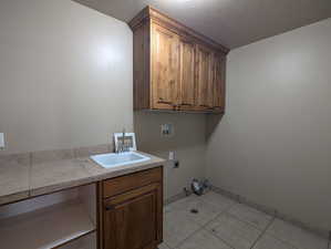 Washroom featuring hookup for an electric dryer, light tile patterned floors, washer hookup, cabinet space, and a sink