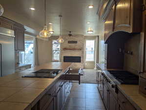 Kitchen featuring black electric stovetop, tile counters, a ceiling fan, a wealth of natural light, and stainless steel gas cooktop