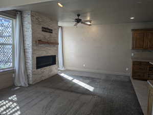 Unfurnished living room featuring baseboards, a fireplace, visible vents, ceiling fan, and light colored carpet