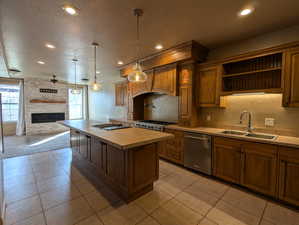 Kitchen with dishwasher, a sink, a textured ceiling, a fireplace, and tile counters
