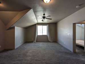 Primary bedroom featuring ceiling fan, a textured ceiling, carpet flooring, and lofted ceiling