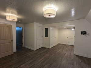 Basement with baseboards, a textured ceiling, electric panel, and dark wood finished floors