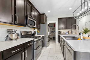 Kitchen with sink, dark brown cabinets, stainless steel appliances, and decorative light fixtures