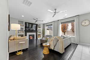 Living room with a fireplace, ceiling fan, built in features, and wood-type flooring