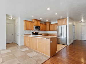 Kitchen with light wood-type flooring, kitchen peninsula, sink, a textured ceiling, and appliances with stainless steel finishes