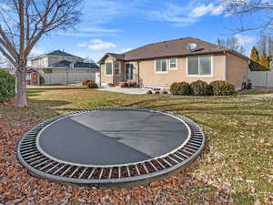 Rear view of property featuring a trampoline and a lawn