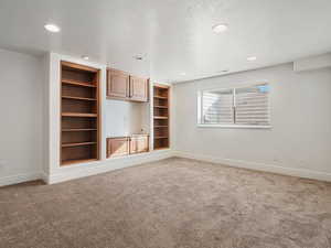 Carpeted spare room featuring built in shelves and a textured ceiling