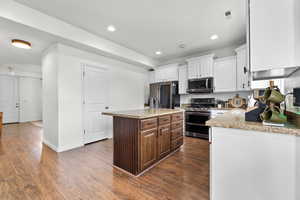 Kitchen featuring a center island, light stone counters, appliances with stainless steel finishes, white cabinets, and dark hardwood / wood-style floors