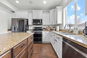 Kitchen with white cabinets, stainless steel appliances, light stone countertops, and sink