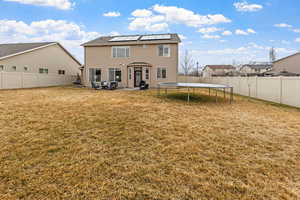 Back of house featuring a patio, a trampoline, a lawn, and solar panels