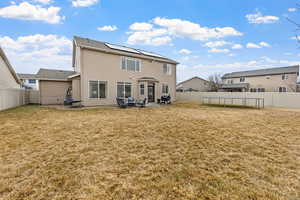 Back of property with a yard, a trampoline, solar panels, and a patio