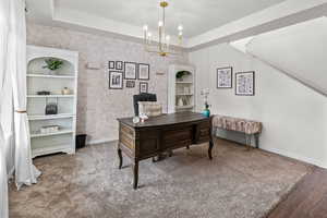 Carpeted office space featuring a notable chandelier and a raised ceiling