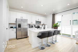 Kitchen featuring sink, stainless steel appliances, an island with sink, and white cabinets