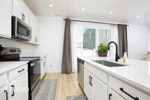 Kitchen with sink, appliances with stainless steel finishes, white cabinets, and light wood-type flooring