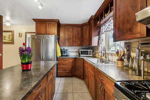 Kitchen featuring stainless steel appliances, range hood, sink, backsplash, and light tile patterned flooring